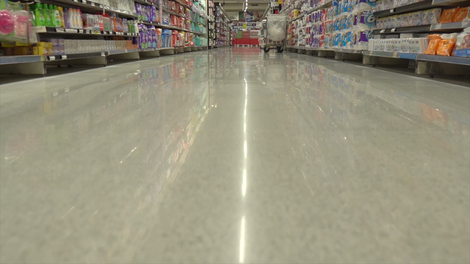 Corredor de supermercado com o piso espelhado refletindo as prateleiras, filmado rente ao chão