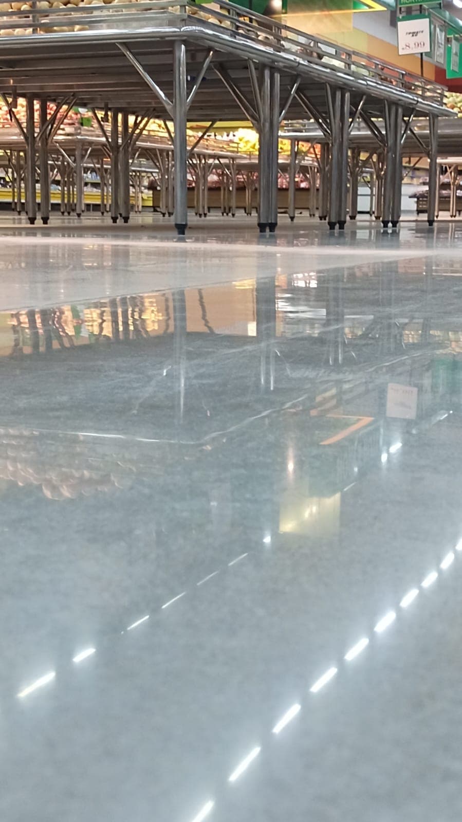 Close rasante do piso sob bancas metálicas, com reflexo nítido das luzes