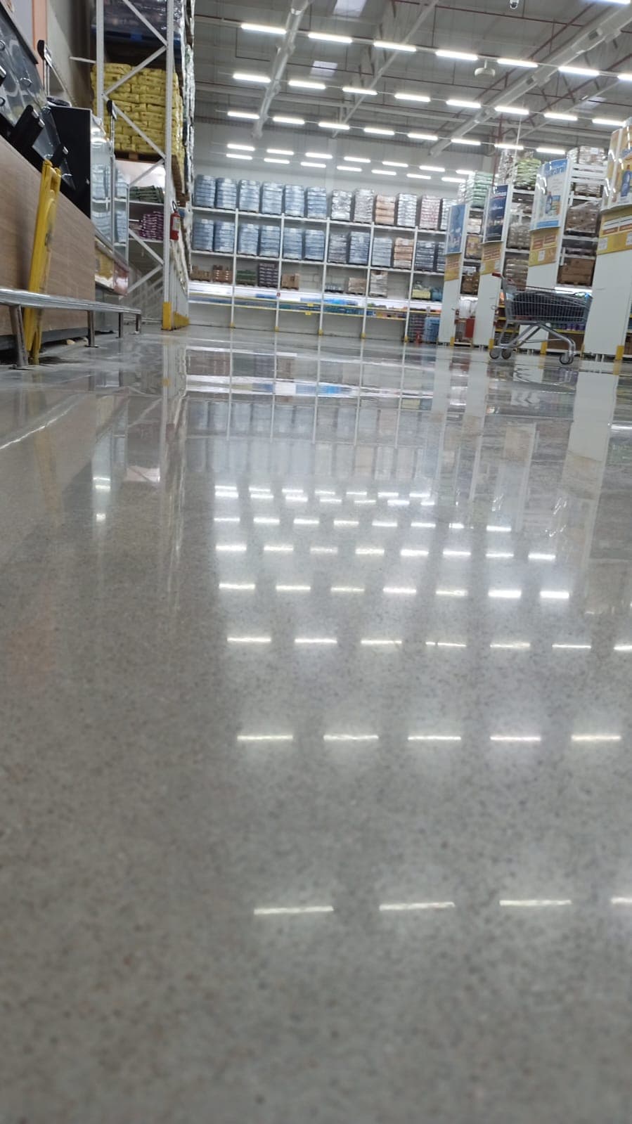 Fileiras de luminárias refletidas em grade no piso de concreto de um atacarejo