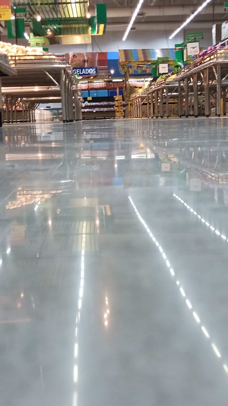 Setor de hortifruti com duas linhas de LED refletidas no piso brilhante